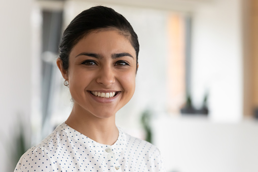 Head shot portrait of confident successful smiling Indian businesswoman standing in office, happy entrepreneur employee executive looking at camera, posing for corporate photo, profile picture