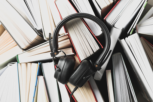 Headphones on many books background, top view