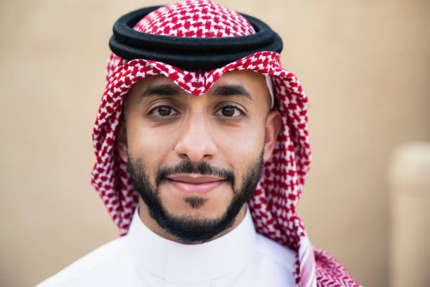 Headshot of bearded Saudi man in traditional attire Close-up of Middle Eastern man in dish dash, kaffiyeh, and agal standing outdoors and looking at camera with contented expression. saudi arabia photos stock pictures, royalty-free photos & images