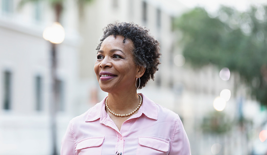 Headshot of a mature black woman walking outdoors in the city, smiling confidently, looking away from the camera.