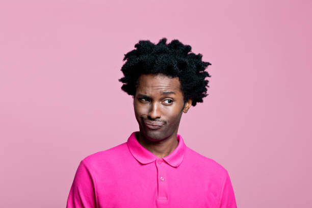 Headshot of surprised young man wearing pink polo shirt Summer portrait of uncertain afro american young man wearing pink polo shirt, looking away. Studio shot on pink background. worried man funny stock pictures, royalty-free photos & images
