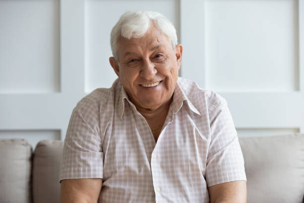 Headshot portrait of smiling mature man relaxing on sofa Close up headshot portrait of smiling mature man sit on couch at home look at camera posing for picture, happy positive senior male or optimistic grandfather feel good relax on comfortable sofa 70 79 years stock pictures, royalty-free photos & images