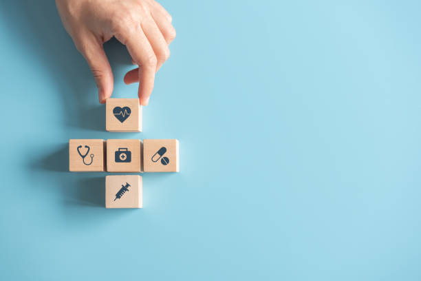 医療保険コンセプト、パステルブルーの背景に医療シンボルを持つ木製キューブを手で配置、コピースペース。 - healthcare ストックフォトと画像