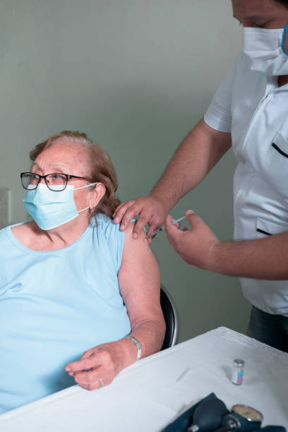 health personnel middle-aged Latino man vaccinating older Latino woman in times of pandemic stock photo