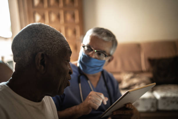 посетитель здравоохранения и старший человек во время домашнего визита - с помощью цифрового планшета - at home covid test стоковые фото и изображения