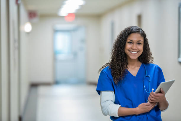 Healthcare worker standing in hospital hallway holding a digital tablet Healthcare worker standing in hospital hallway holding a digital tablet female nurse stock pictures, royalty-free photos & images