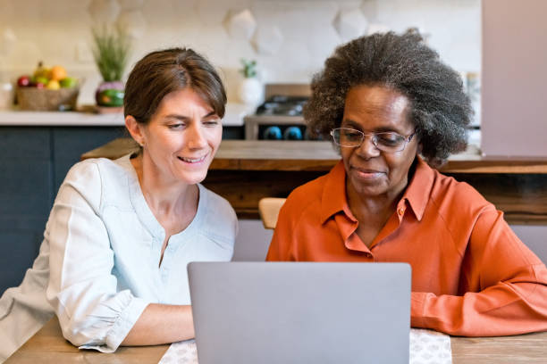 Healthcare worker teaching laptop to senior woman Caregiver teaching laptop to senior woman. Elderly female is wearing eyeglasses. They are at home. social work online stock pictures, royalty-free photos & images