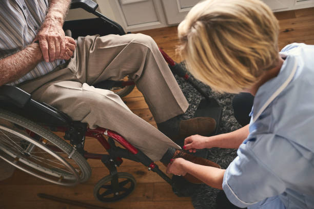 Healthcare worker tie shoe laces of disabled senior man Female healthcare worker helping disabled senior man in wheelchair, tie shoe laces. getting dressed stock pictures, royalty-free photos & images