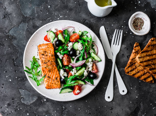 Healthy balanced lunch - grilled red fish fillet salmon and vegetables, olives, feta salad on dark background, top view stock photo