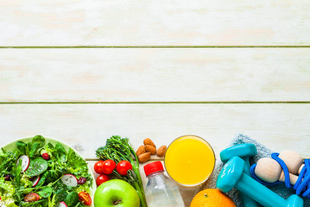 Healthy eating and exercising backgrounds: Top view of a fresh organic salad plate, orange juice glass, almonds, green apple, dumbbells, jumping rope, towel, water bottle placed in a row at the bottom border of an horizontal frame leaving useful copy space for text and/or logo. Predominant color is green. High key DSRL studio photo taken with Canon EOS 5D Mk II and Canon EF 100mm f/2.8L Macro IS USM.