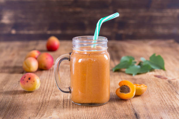 Healthy eating, food, dieting and vegetarian concept - smoothie from apricot and peach in glass mug. Fresh apricot and juice on wooden background Healthy eating, food, dieting and vegetarian concept - smoothie from apricot and peach in glass mug, close up. Fresh apricot and juice on wooden background peach smoothie stock pictures, royalty-free photos & images