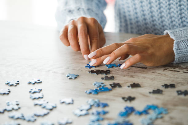Healthy entertainment during self isolation times Close up of female hands playing with puzzle pieces on wooden table to spend lockdown time in a healthy entertaining way. puzzle stock pictures, royalty-free photos & images