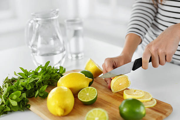 Healthy Food And Eating. Closeup Of Woman Kitchen Cutting Lemons Healthy Food And Eating. Closeup Of Woman In The Kitchen Cutting Lemons And Limes. Healthy Lifestyle. Citrus Fruits. Vitamin C. Detox Water. Lemonade. Diet. Dieting Concept. detox stock pictures, royalty-free photos & images
