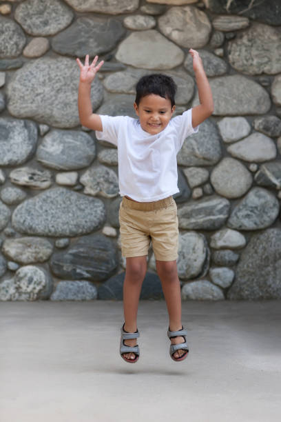 A healthy four year old boy tries to jump as high off the ground as he can. stock photo