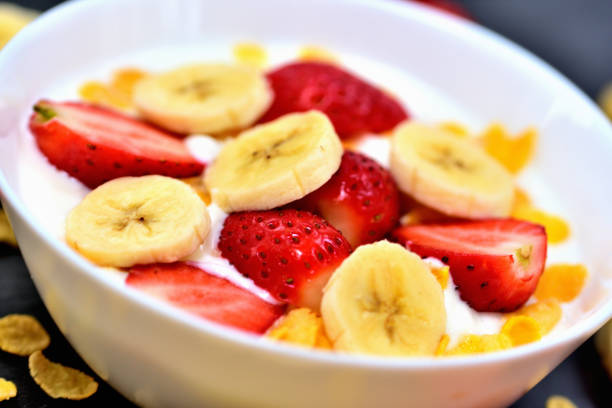 Healthy fruit bowl with yogurt, banana, strawberries and cornflakes. Glass jugs with cow milk. Close-up. stock photo