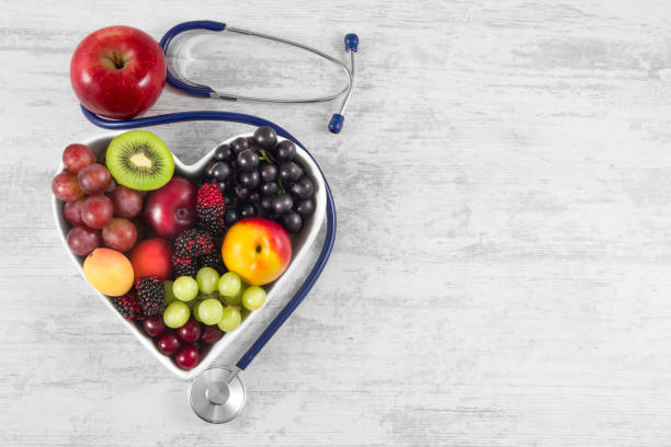 Kesehatan jantung, dan konsep diet kolesterol. Buah-buahan sehat dalam mangkuk berbentuk hati dengan stetoskop dan apel hijau di atas meja kayu vintage putih.