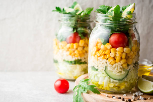 Healthy homemade salads with bulgur, vegetables and lime in mason jars on grey stone background. stock photo
