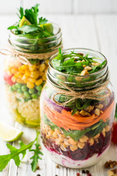 Healthy homemade salads with chickpeas, bulgur and vegetables in mason jars on white wooden background. stock photo