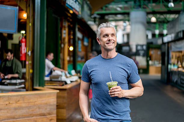 Healthy man having a smoothie Healthy man drinking a smoothie and walking on the street looking happy drinking smoothie stock pictures, royalty-free photos & images
