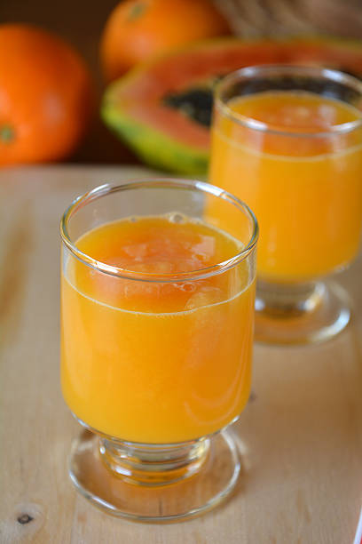 Healthy orange, papaya and ginger smoothie. Glass of orange and papaya smoothie on a wooden table. Closeup. papaya smoothie stock pictures, royalty-free photos & images