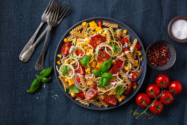 healthy pasta salad with zucchini sweet corn tomato and basil, vegetarian lunch stock photo