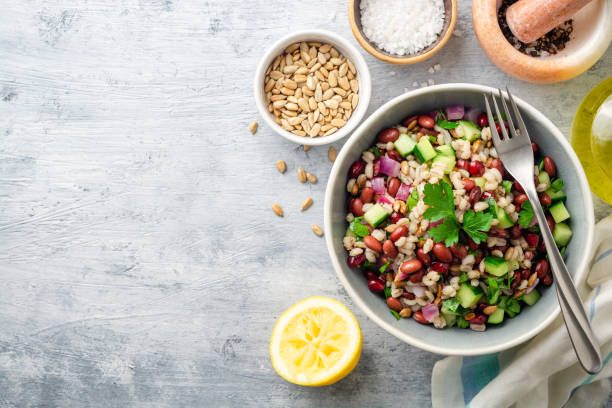 Healthy pearl barley salad with beans, cucumbers, red onion, sunflower seeds, pomegranate and parsley in bowl on concrete background stock photo
