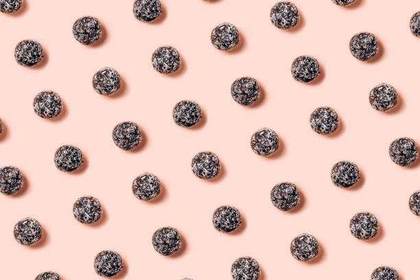 Healthy raw energy balls made of dried fruits and nuts with coconut chips, flax seeds, pistachios, sesame. Pattern on pink background stock photo