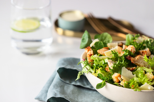 Healthy salad with  different lettuce, croutons,cheese,  chicken and dressing with especial sauce. Caesar salad in the white plate served with glass water and gold cutlery on the restaurant table.
