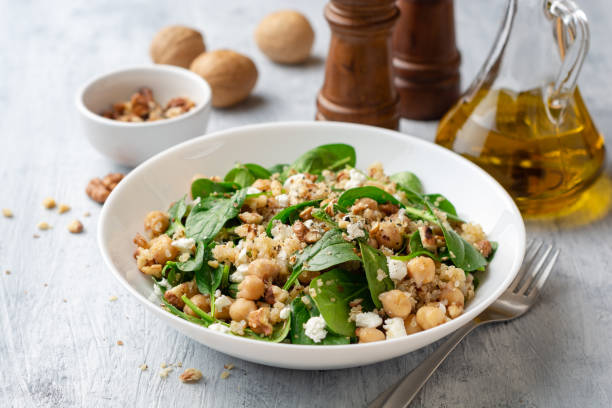 Healthy salad with spinach, chickpeas, quinoa, feta cheese and walnuts in white plate on concrete background stock photo