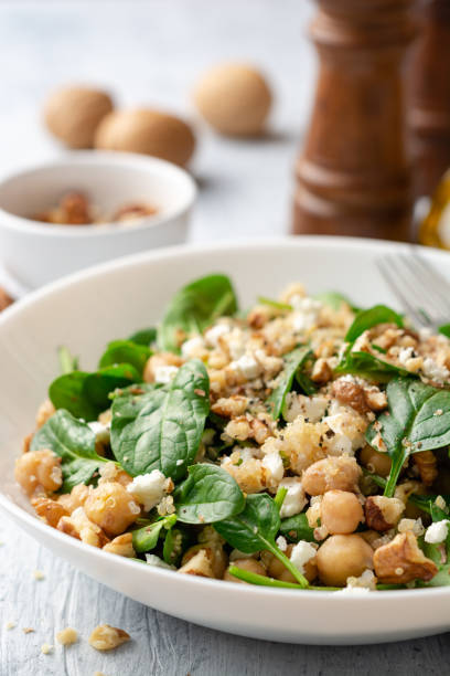 Healthy salad with spinach, chickpeas, quinoa, feta cheese and walnuts in white plate on concrete background stock photo