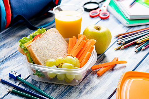 Healthy food for kids concepts: well balanced school lunch box shot on blue table. School supplies are around the lunch box. High resolution 42Mp studio digital capture taken with SONY A7rII and Zeiss Batis 40mm F2.0 CF lens