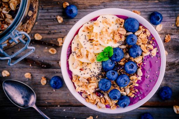 healthy smoothie bowl with granola, banana and fresh blueberries healthy smoothie bowl with granola, banana and fresh blueberries on wooden background bowl stock pictures, royalty-free photos & images