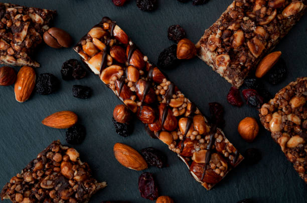 Healthy snacks, fitness lifestyle and high fiber diet concept with granola energy bars surrounded by dried fruits, hazelnuts and almonds on a black stone with dramatic light stock photo