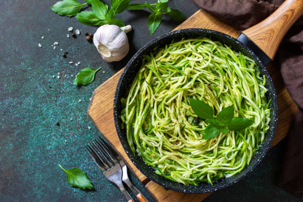 Healthy vegan food, low carb dish. Cooked zucchini noodles with basil and garlic in a cast iron pan on a stone countertop. Top view flat lay background. Copy space. stock photo
