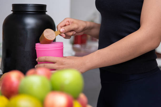 gezonde vrouwen bereiden een proteïne van de wei na het doen van krachttraining in de keuken met vers fruit als een wazig voorgrond. - eiwit organische verbinding stockfoto's en -beelden