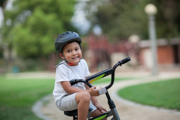 A healthy young boy sitting on his bike on a park trail who is wearing a safety helmet, t-shirt and shorts. stock photo