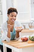 Confident young woman eats a bowl of healthy granola for breakfast. A bowl of strawberries and a green salad are on the counter in front of her.