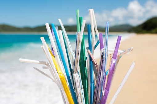 Heap of used plastic straws on background of clean tropical beach and ocean waves