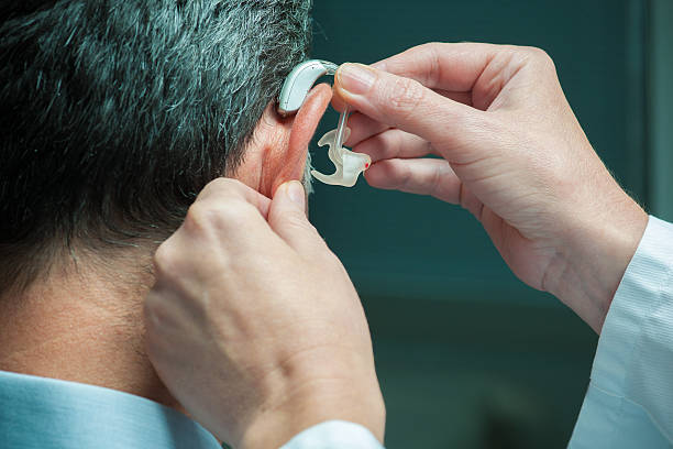 Hearing Aid Doctor inserting hearing aid in man's ear hearing aids stock pictures, royalty-free photos & images