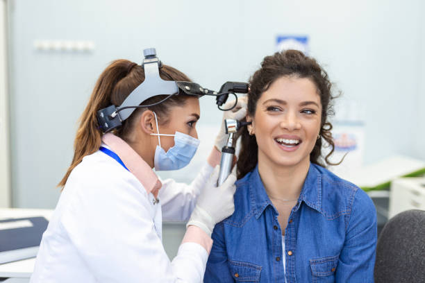 Hearing exam. Otolaryngologist doctor checking woman's ear using otoscope or auriscope at medical clinic. Otorhinolaryngologist pulling ear with hand and looking at it with otoscope closeup. stock photo