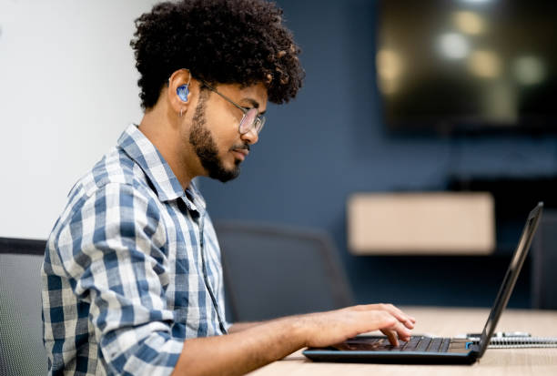 слабослышащий мужчина, работающий на ноутбуке в офисе - hearing aid стоковые фото и изображения