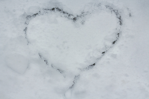 A heart drawn on a background covered with first snow.