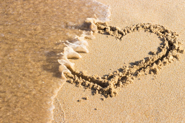 heart drawn on sand is washed off by sea wave, top view End relationship. stock photo