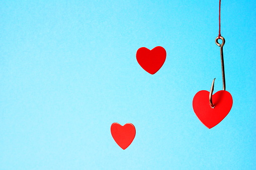 Heart on a hook on a blue background. A metal fishhook hanging from a rope pierced the red cardboard heart. Concept of love. Valentine's day. Love choice. Three hearts and one hook.