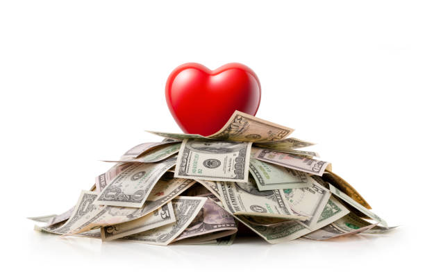 Heart on top of a pile of dollar bills stock photo