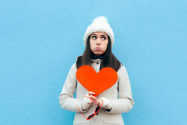 ragazza sconvolta dal cuore triste che tiene un cuore su sfondo blu - san valentino single foto e immagini stock
