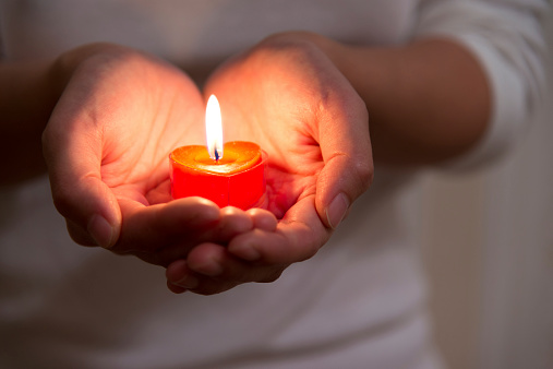 Woman hands holding burning heart-shaped candle. Symbol of hope, peace and love.