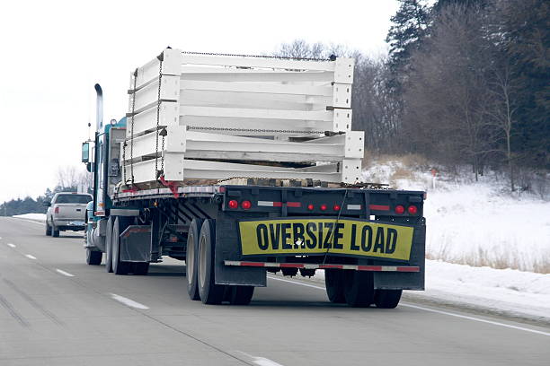 Heavy Haul Trucks deliver the goods all across the world. Here a truck with an "OVERSIZE LOAD" (wider than 12') travels down a four-lane highway in winter. Good for illustrating delivery in adverse conditions, getting the job done no matter what, or any delivery/trucking related. oversized object stock pictures, royalty-free photos & images