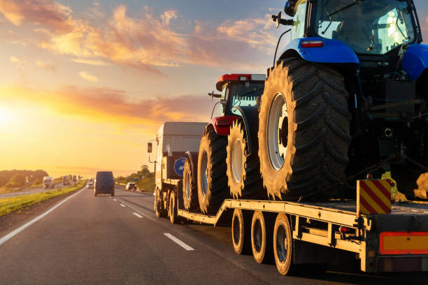 POV heavy industrial truck semi trailer flatbed platform transport two big modern farming tractor machine on common highway road at sunset sunrise sky. Agricultural equipment transportation service stock photo