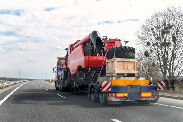 Heavy industrial truck with semi trailer platform transport disassembled combine harvester machine on common public highway road on sunset sunrise day. Agricultural equipment transportation service stock photo